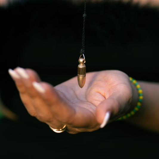 A person holding a pendulum in their hand, with a focus on the pendulum and a black string attached to it. The person is wearing a black dress and has a manicure.