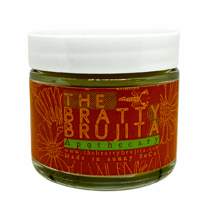 Glass jar with white lid with red/prange label and orange writing 'The Bratty Brujita Apothecary' product on a white background